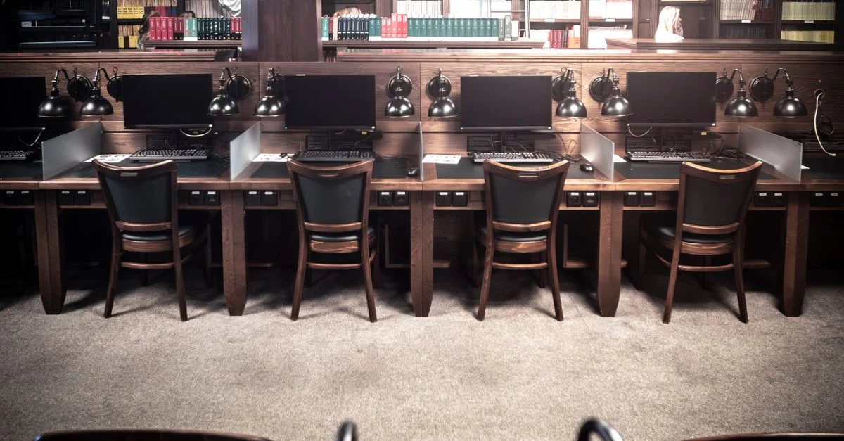 Postes de travail de bibliothèque vides, équipés d'ordinateurs et de lampes vintage, idéaux pour l'étude ou la recherche.