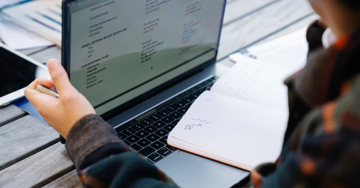 Gros plan sur des mains utilisant un ordinateur portable et prenant des notes sur une table en bois.