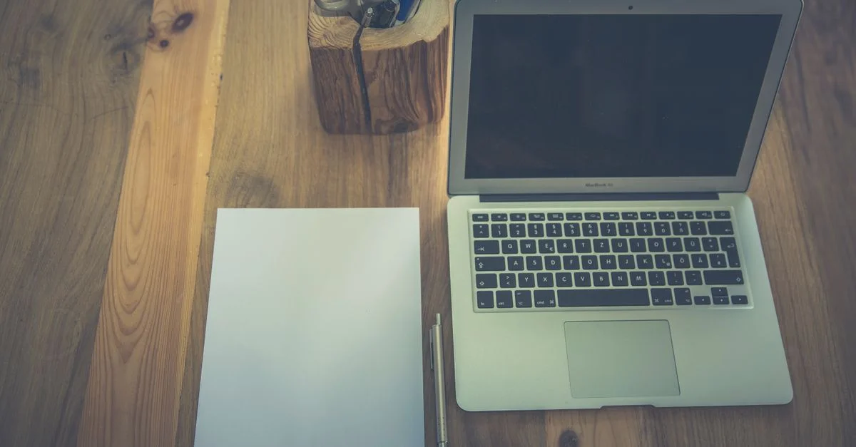 Un espace de travail minimaliste avec un ordinateur portable, du papier et des fournitures de bureau sur un bureau en bois.
