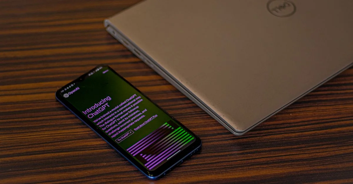 Un smartphone affichant l'application ChatGPT à côté d'un ordinateur portable fermé sur une table en bois.