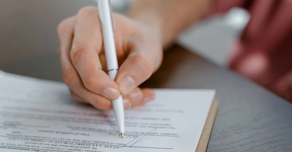 Vue détaillée d'une main écrivant une signature sur un document officiel avec un stylo à bille.