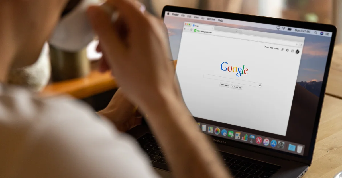 Gros plan d'un adulte buvant du café et naviguant sur Google sur un ordinateur portable à l'intérieur.